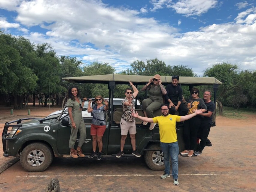 Grande grupo de turistas posando com veículo de safári verde com toldo de lona em savana